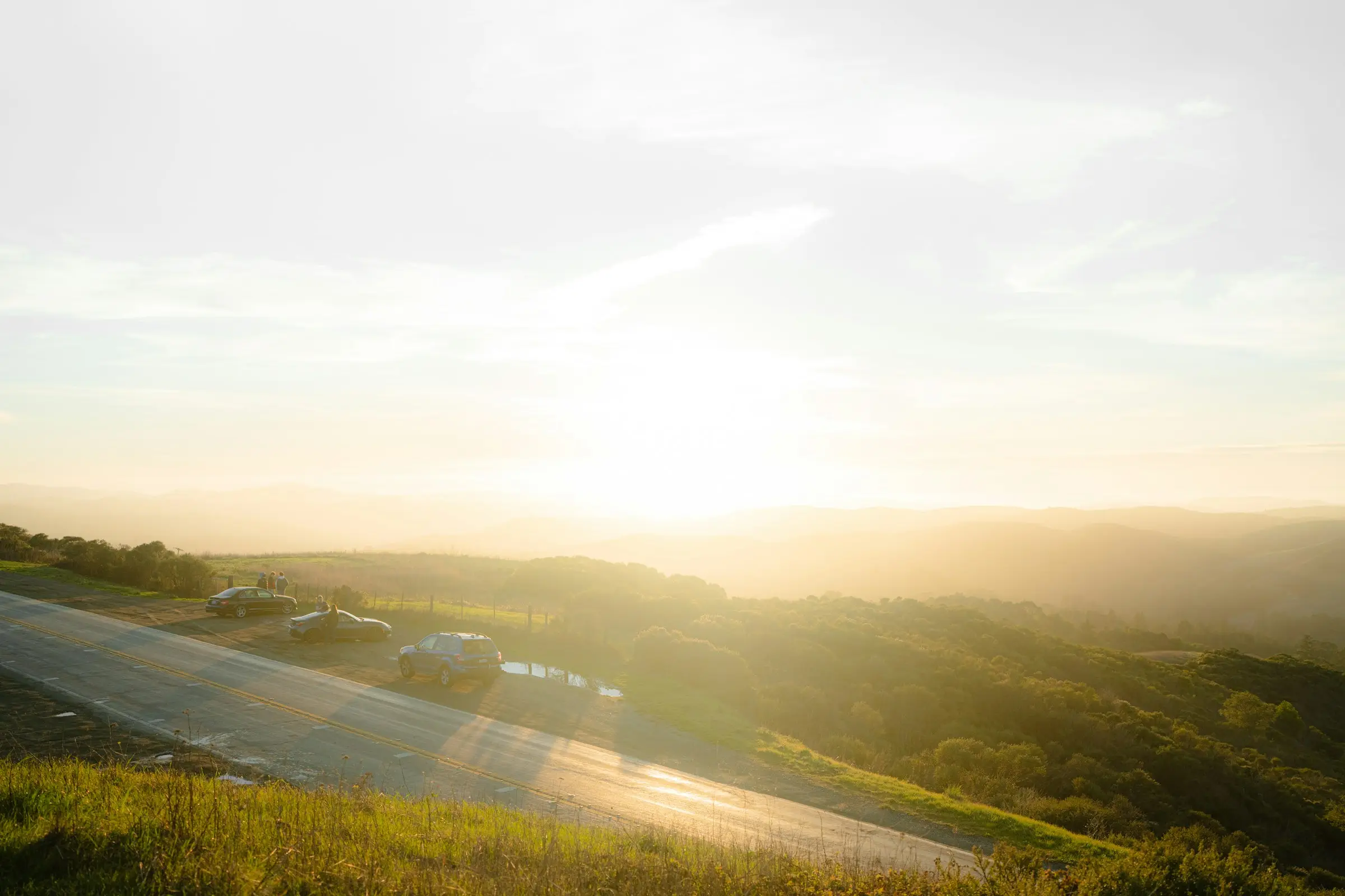 A road winding through hills at golden hour, with the sun low over the horizon