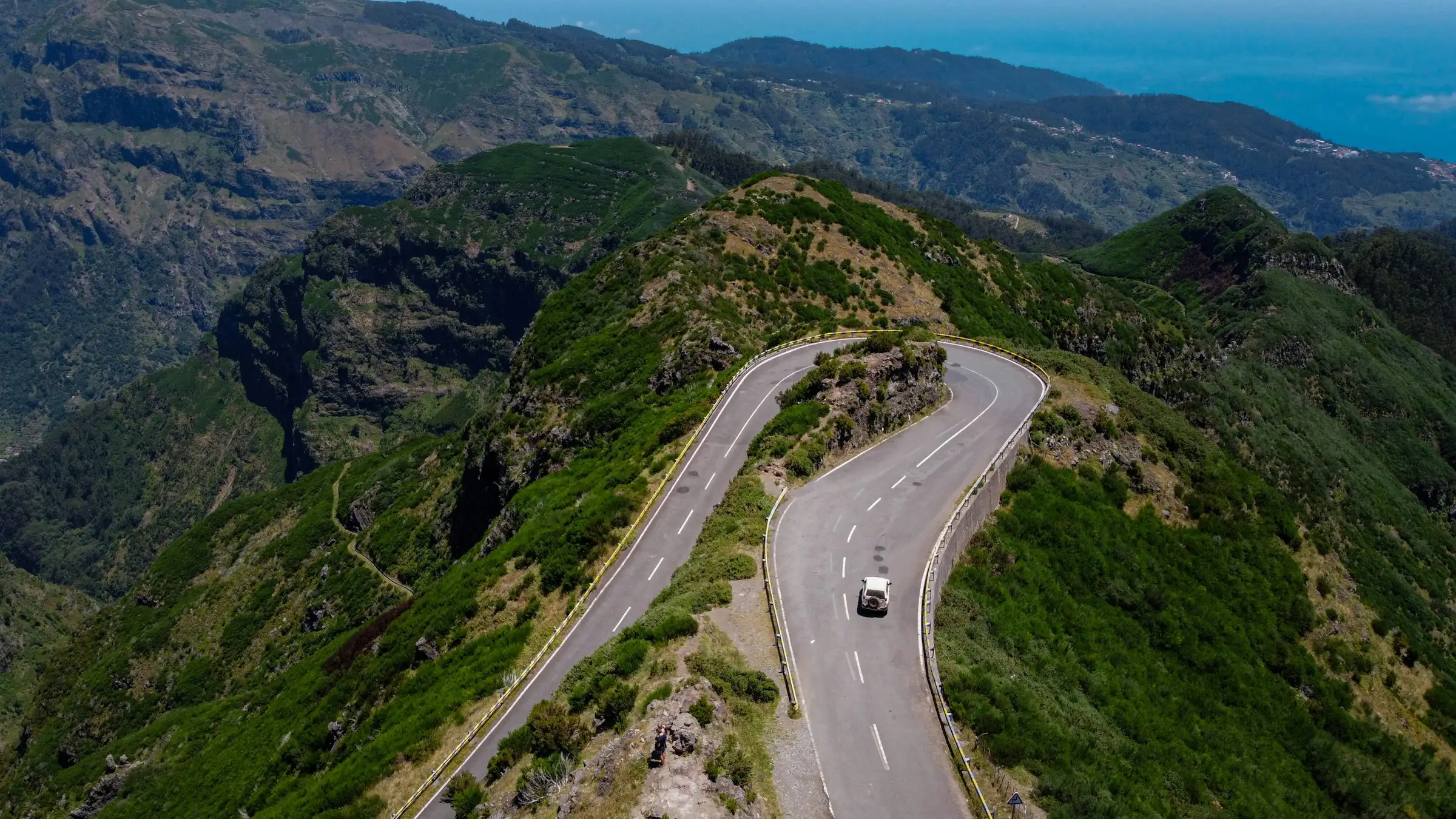 A mountain road with tight switchbacks seen from above, one car on the road